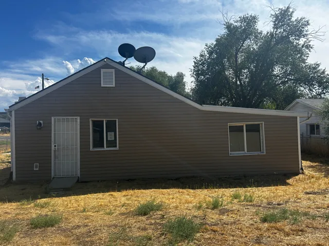 Rear exterior. Brown horizontal siding exterior with a white gable vent, a window with white trim, and a white security screen door