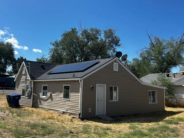 Exterior featuring solar panels, beige siding, white trim windows, and a dark shingle roof