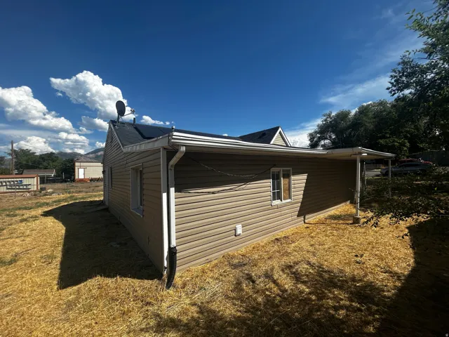 Beige siding exterior with a covered side patio, white framed windows, and a dark shingle roof