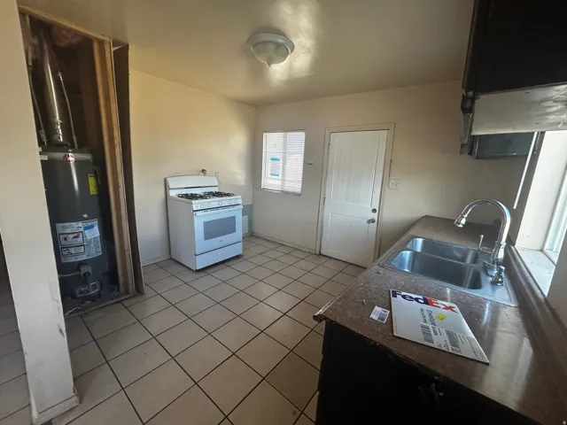 Kitchen with tiled flooring, a stainless steel double-basin sink, and a white freestanding gas range