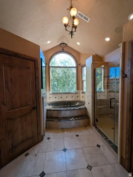 Primary bath with soaking tub with tiled surround, arched window, and adjacent glass-enclosed shower