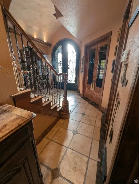 Arched entry door with decorative ironwork, wrought iron staircase railing with wood handrail, tiled flooring with accent inlays, and paneled wood doors