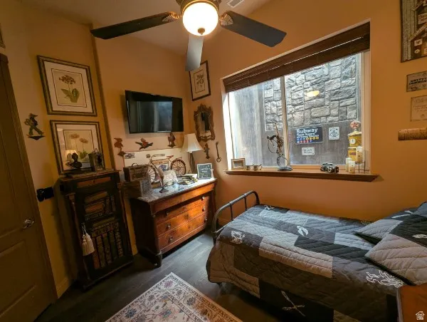 Basement bedroom wint wood-finish flooring, ceiling fan, and a large window with a wood sill