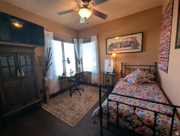 Bedroom wood-finish flooring, ceiling fan with integrated lighting, multiple windows with blinds, and built-in cabinetry