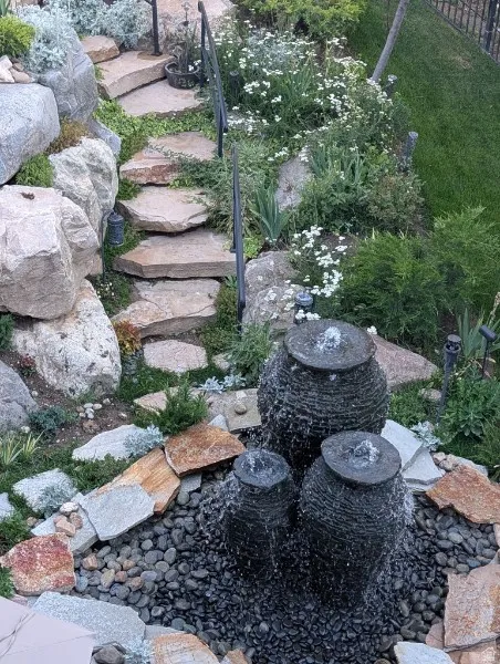 Terraced landscaping featuring a multi-tiered water feature, natural stone steps, decorative rock accents, and established plantings