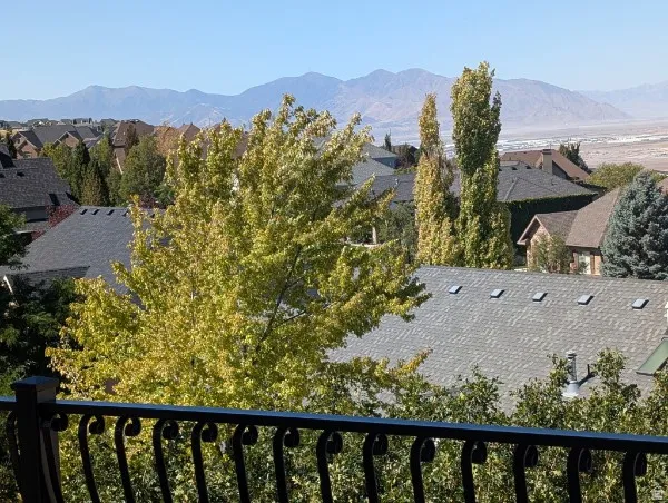Decorative wrought iron railing, expansive mountain backdrop, distant city horizon, mature deciduous trees, neighborhood rooftops