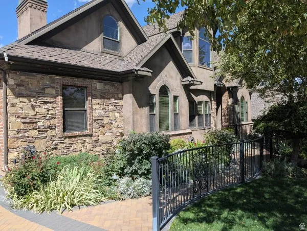Stone and stucco exterior detailing, arched windows, brick paver walkway, ornamental wrought iron fencing, and mature landscaping
