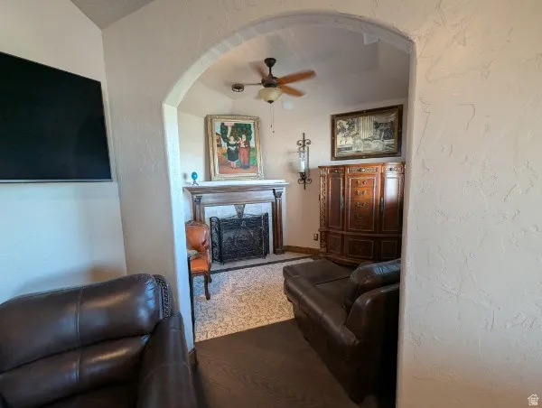 Arched entryway leading to athe primary bedroom featuring a fireplace with a decorative screen and an ornate mantel, a ceiling fan, and a built-in wood cabinet