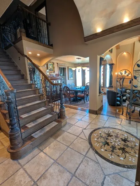Grand entryway featuring a decorative mosaic floor inlay, a sweeping staircase with ornate wrought iron and wood balusters, and arched doorways