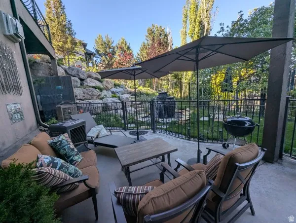 Expansive concrete patio with a black metal fence, rock retaining wall, and mature landscaping