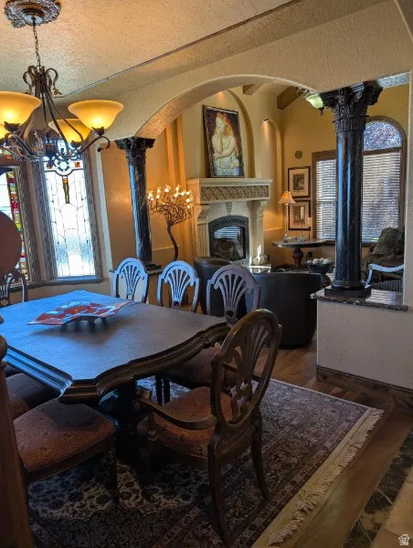 Arched entryway with decorative columns, ornate chandelier, decorative stained glass window, fireplace with mantel, and wood-finish flooring