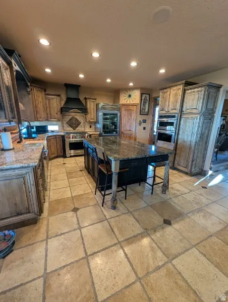 Gourmet kitchen featuring a large central island, granite countertops, custom cabinetry, stainless steel appliances, and tiled flooring