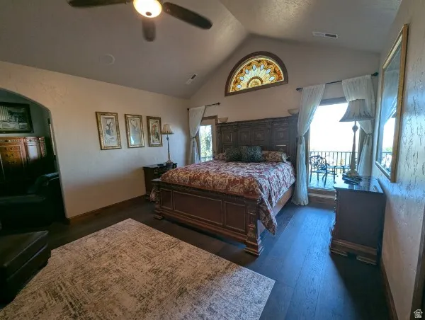 Primary bedroom with vaulted ceiling with a ceiling fan, dark wood-finish flooring, half-round stained glass window, and a private balcony
