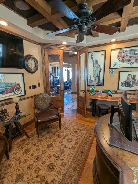 Wood-finish flooring with a decorative area rug, coffered ceiling with a ceiling fan, and recessed lighting