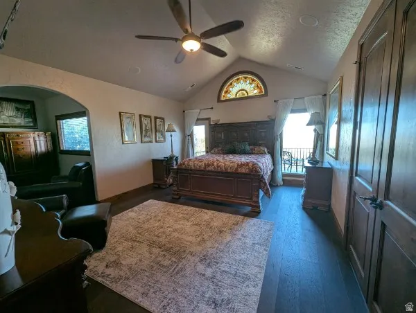 Primary bedroom with vaulted ceiling with an arched window, wood-finish flooring, and a ceiling fan with integrated lighting