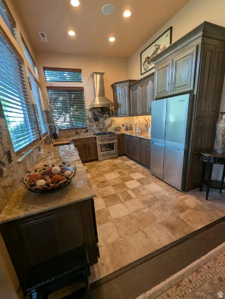 Basement full kitchen featuring recessed lighting, a stainless steel range hood, dark wood-finish cabinetry, and stone-finish countertops