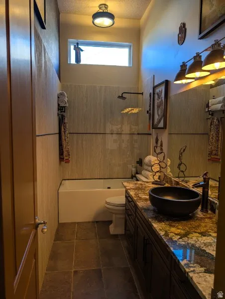 Built-in bathtub with tiled surround, dark wood-finish vanity with stone countertop, black vessel sink, and coordinating dark floor tiling