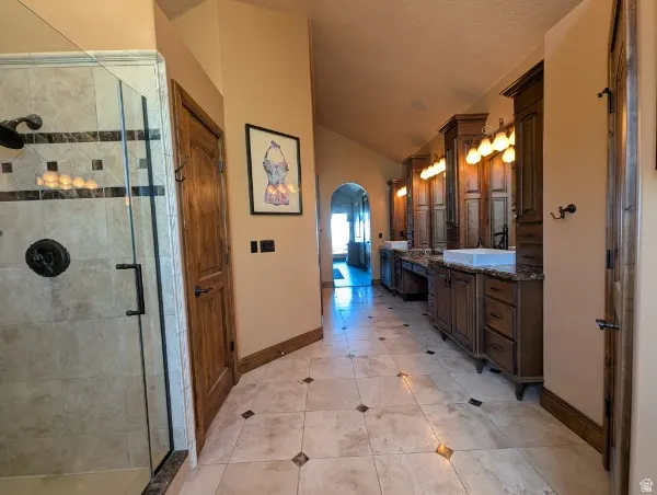 Spacious primary bath featuring a tiled walk-in shower with a glass enclosure, dual vanity cabinetry with vessel sinks, and tiled flooring