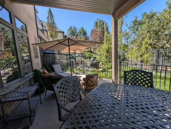 Covered patio featuring an outdoor water feature, a wrought iron fence, a stone retaining wall, and mature landscaping