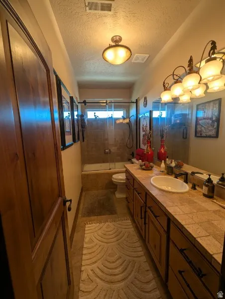 Wood-paneled door, tiled flooring, built-in vanity with dual sinks, tiled countertop, and a shower-tub combination with a glass enclosure