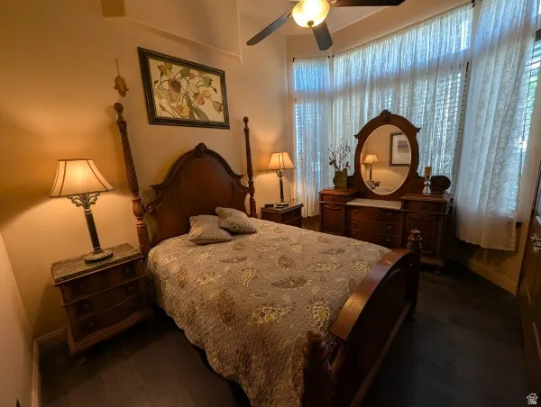Dark wood-finish flooring, bay window with translucent window treatments, and a ceiling fan with integrated lighting