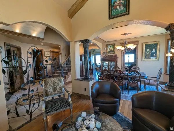 Archways with recessed lighting, exposed wood ceiling beam, decorative metal railings, ornate columns, and wood-finish flooring