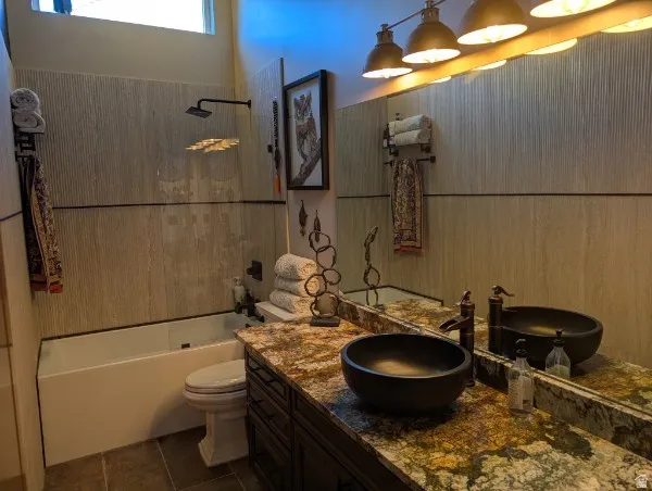 Dual vessel sinks with bronze-finish fixtures, a large vanity mirror, a granite-style countertop, and textured wall tiling