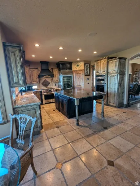 Gourmet kitchen featuring a large central island with bar seating, tiled flooring with accent inlays, built-in stainless steel appliances, recessed ceiling lights, and custom cabinetry