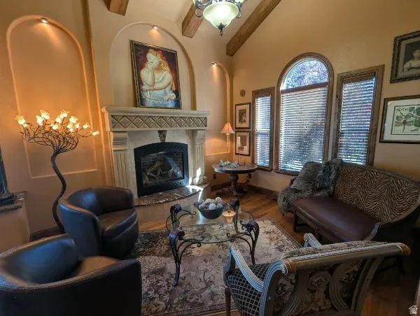 Vaulted ceiling with exposed wood beams, arch-top windows, fireplace with an ornate mantel, wood-finish flooring, and recessed wall niches