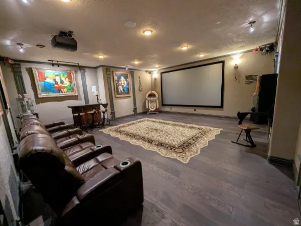 Dedicated entertainment space featuring a large projection screen, recessed lighting, wall sconces, wood-finish flooring, and a built-in bar