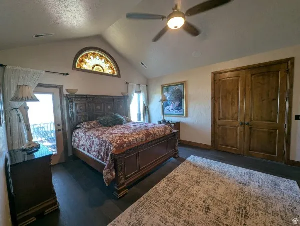 Primary bedroom with vaulted ceiling with a ceiling fan, dark wood-finish flooring, two arched doorways, and a built-in fireplace in an adjacent area