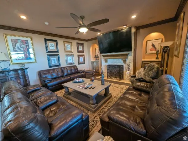 Spacious living area featuring a stone-clad fireplace with an ornate screen, ceiling fan with integrated lighting, recessed lighting, and crown molding