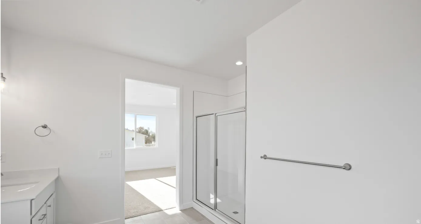 Glass-enclosed shower, white vanity with integrated sink, recessed lighting, and wall-mounted towel bars