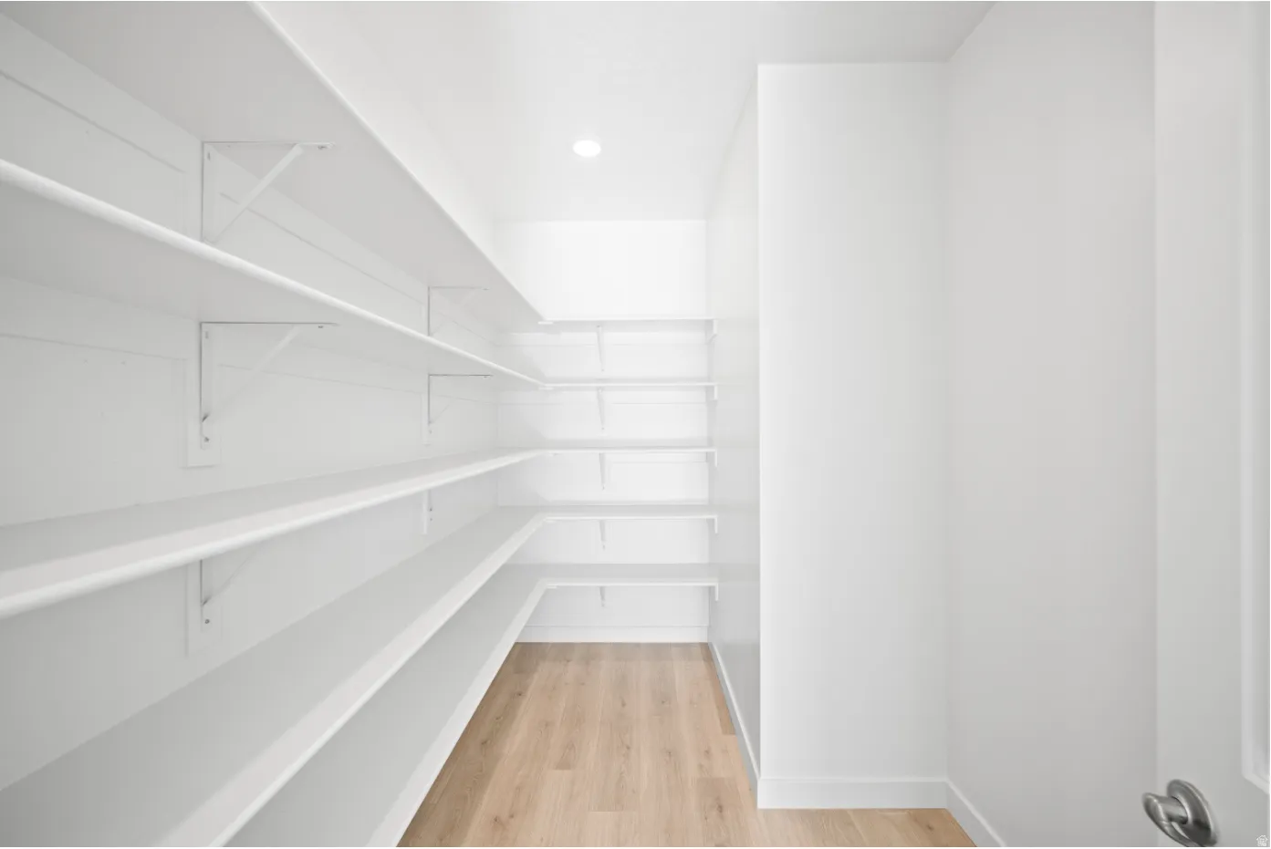 Walk-in pantry featuring extensive white shelving, recessed lighting, and wood-finish flooring