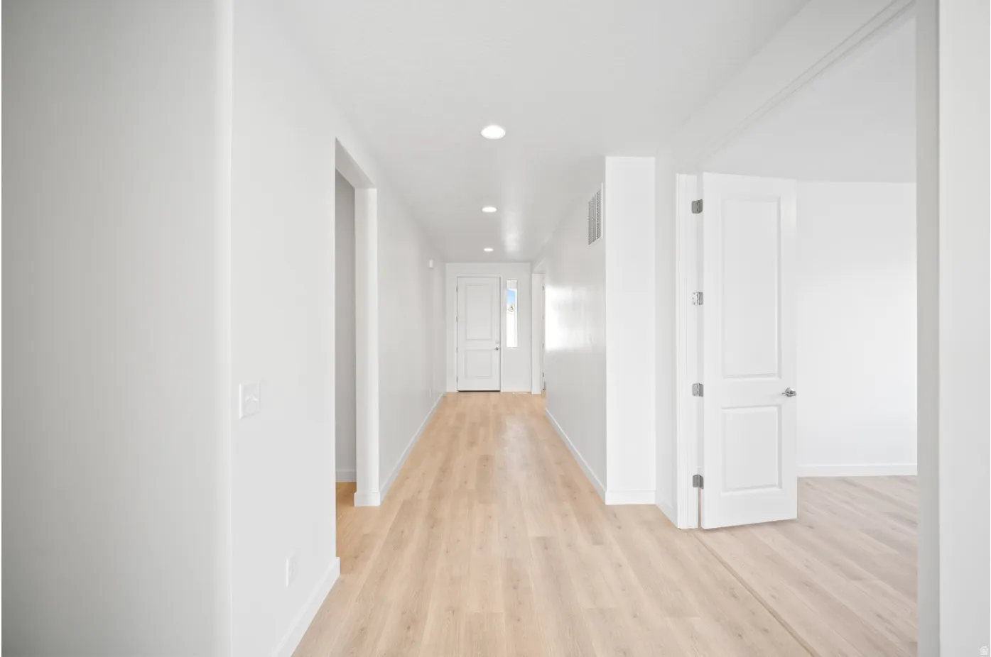 Recessed lighting illuminates the hallway, featuring wood-finish flooring and crisp white walls