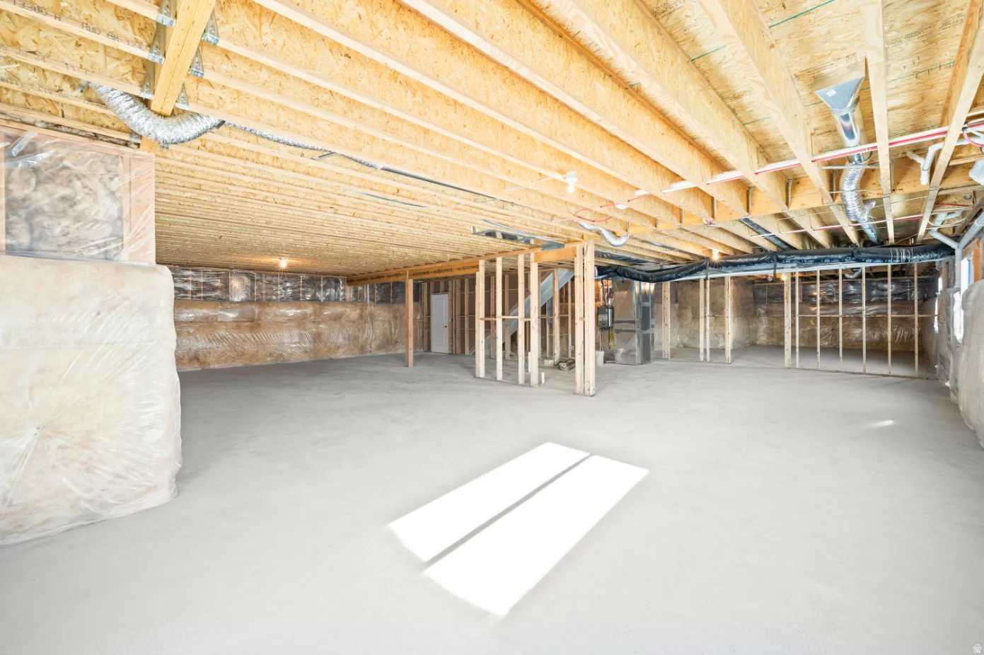 Unfinished basement featuring exposed wood joists, framed interior walls, concrete flooring, and visible ductwork