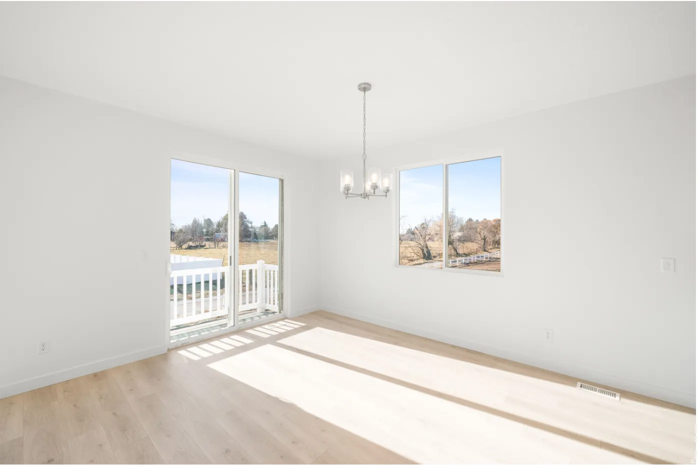 White walls, wood-finish flooring, sliding glass door with a white railing, and a multi-bulb chandelier