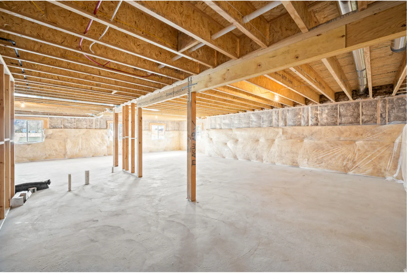 Unfinished basement with exposed ceiling joists, support beams, and a concrete floor
