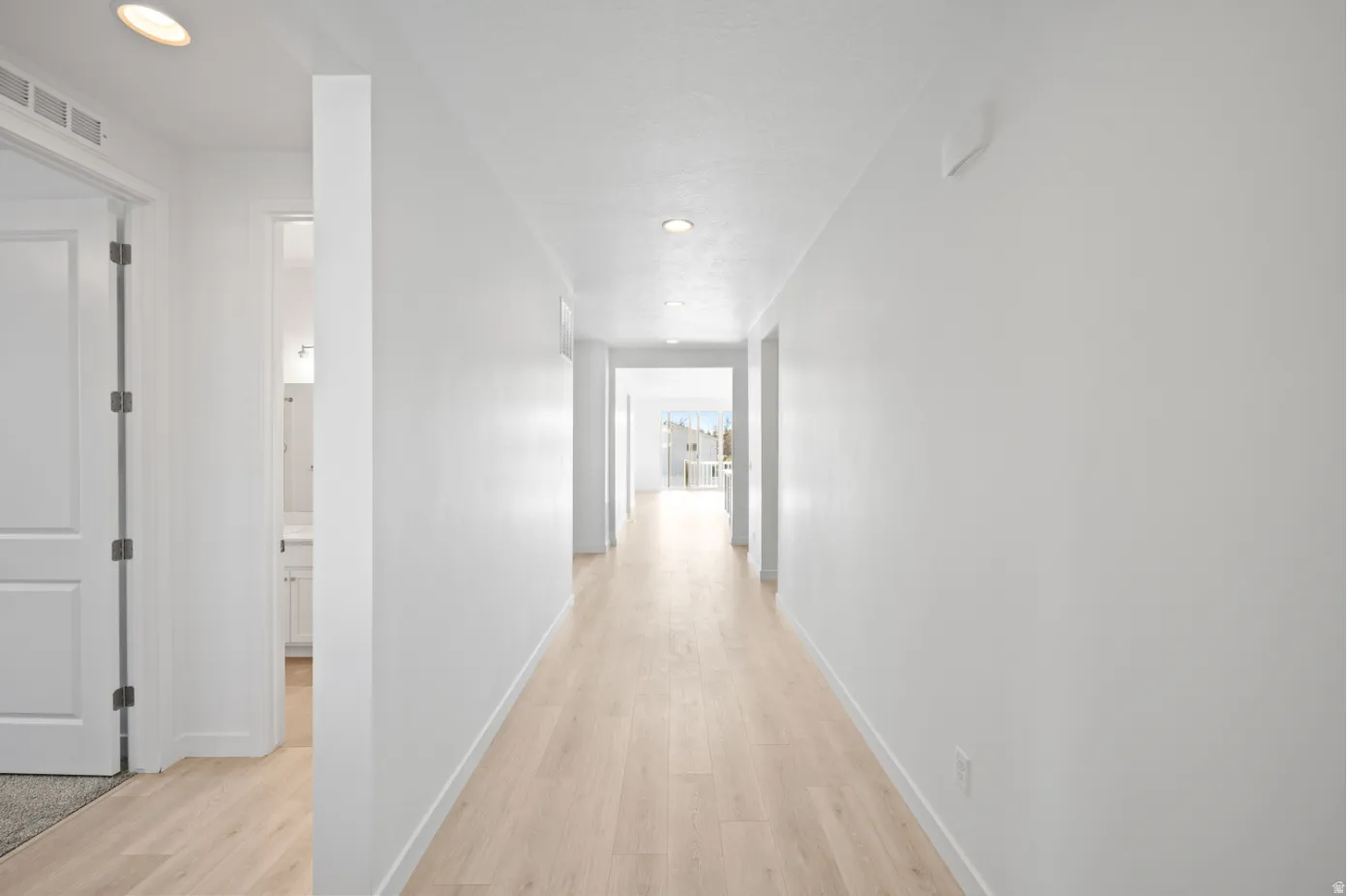 Recessed lighting illuminates the hall, featuring wood-finish flooring and crisp white walls