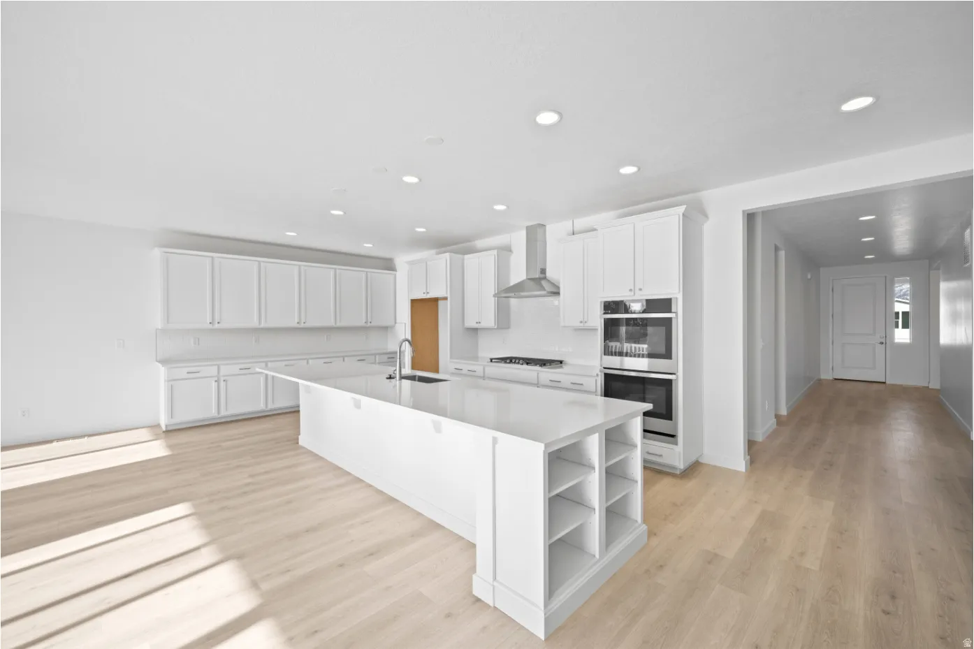 Spacious kitchen featuring an expansive central island with integrated shelving, extensive white cabinetry, light wood-finish flooring, stainless steel appliances, and recessed lighting