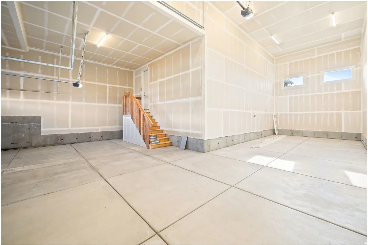 Spacious garage with exposed framing, concrete flooring, overhead lighting, and wood stairs with a railing