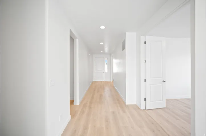 Recessed lighting illuminates the hallway, featuring wood-finish flooring and crisp white walls