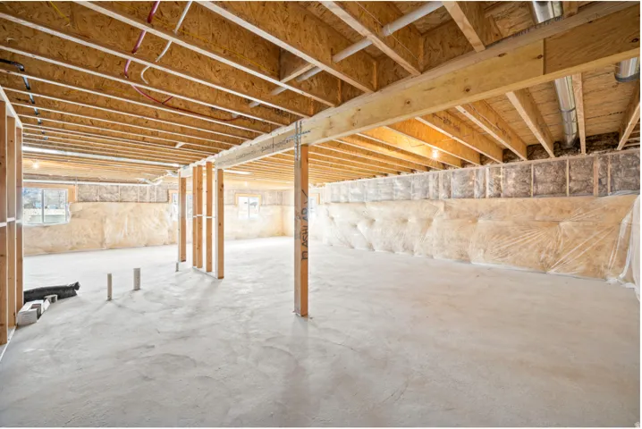Unfinished basement with exposed ceiling joists, support beams, and a concrete floor