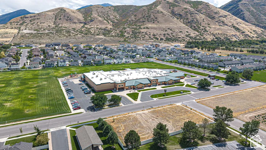 Neighborhood setting with mountain backdrop, residential properties, open green spaces, paved roads, and a large community building