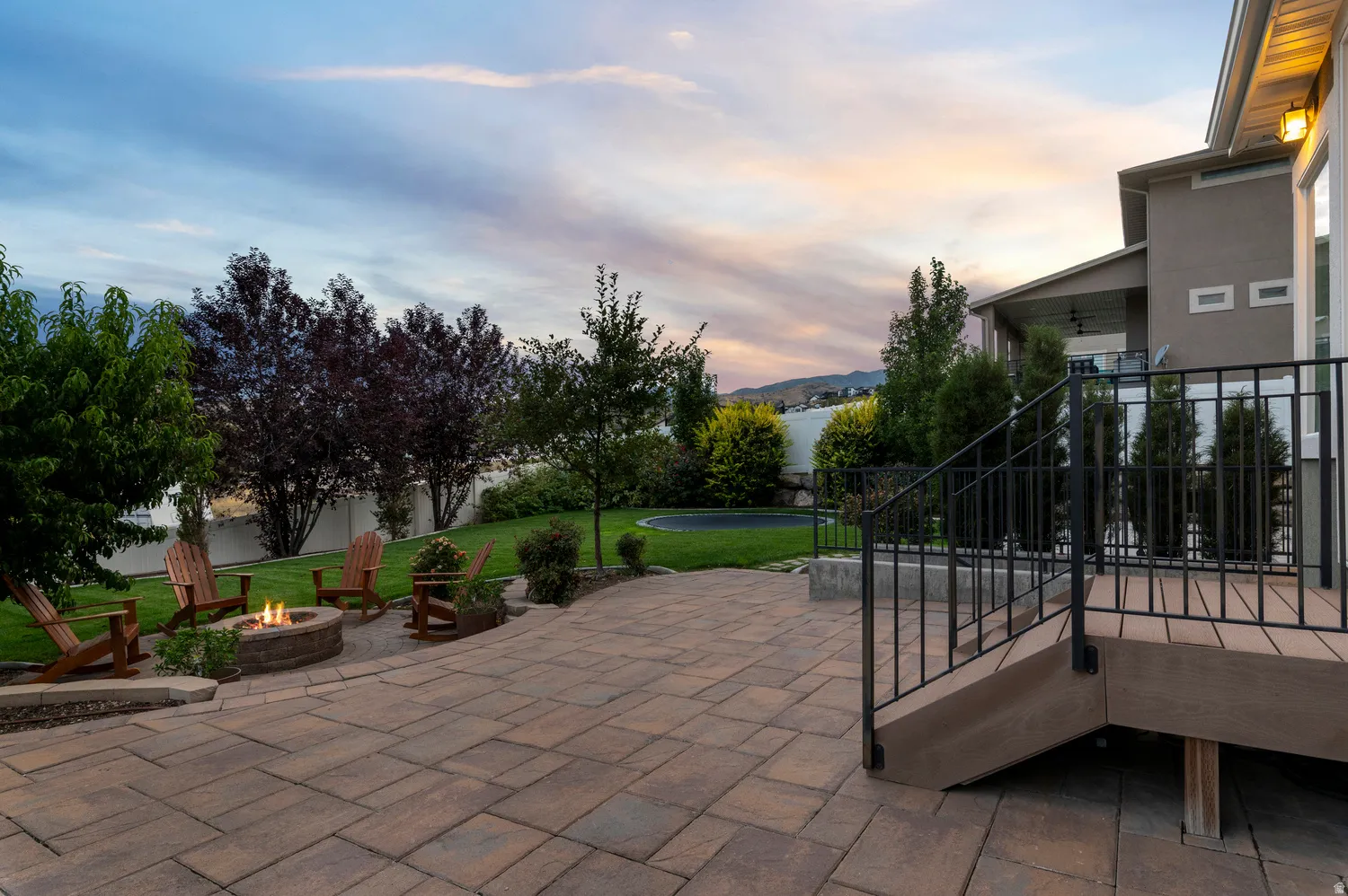 Expansive paver patio with a built-in fire pit, surrounded by a manicured lawn and mature landscaping