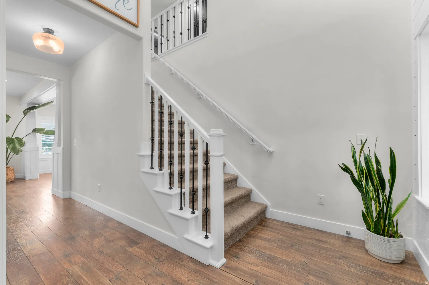 Wood-finish flooring throughout, a carpeted staircase with white risers, and black metal balusters