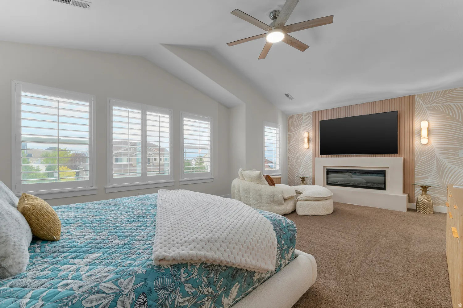 Angled ceiling with a contemporary ceiling fan, multiple windows with white plantation shutters, built-in fireplace with a hearth, accent wall with vertical wood paneling and sconce lighting, and carpeted flooring
