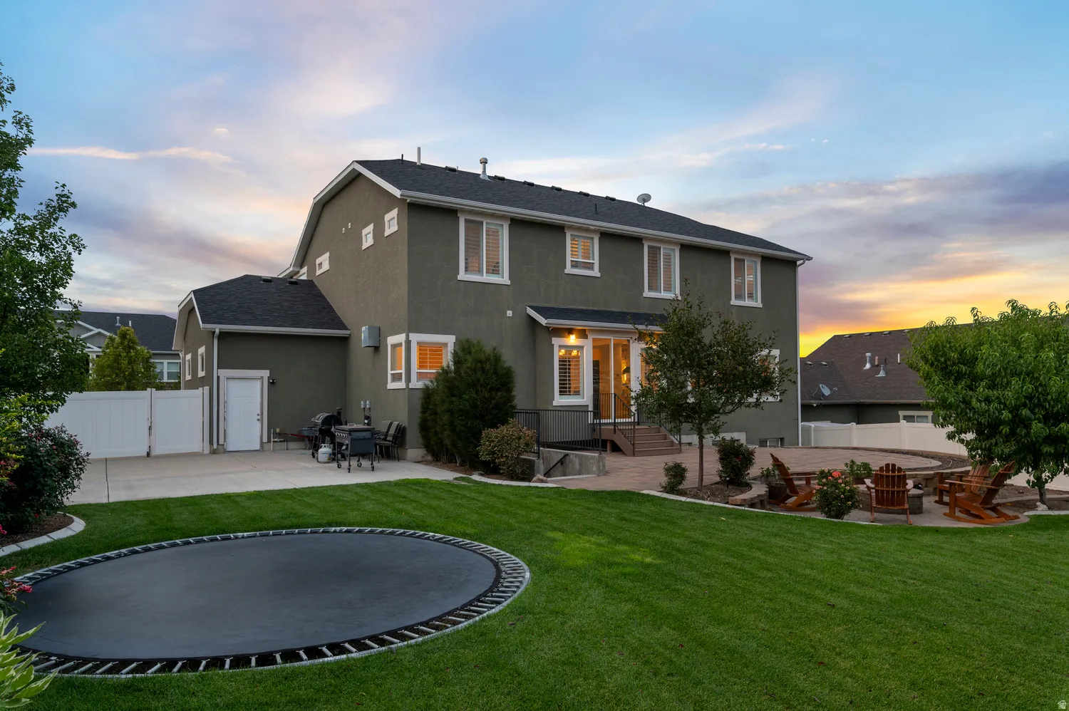 Expansive backyard featuring a large green lawn, paver patio, stone fire pit area, and a white privacy fence