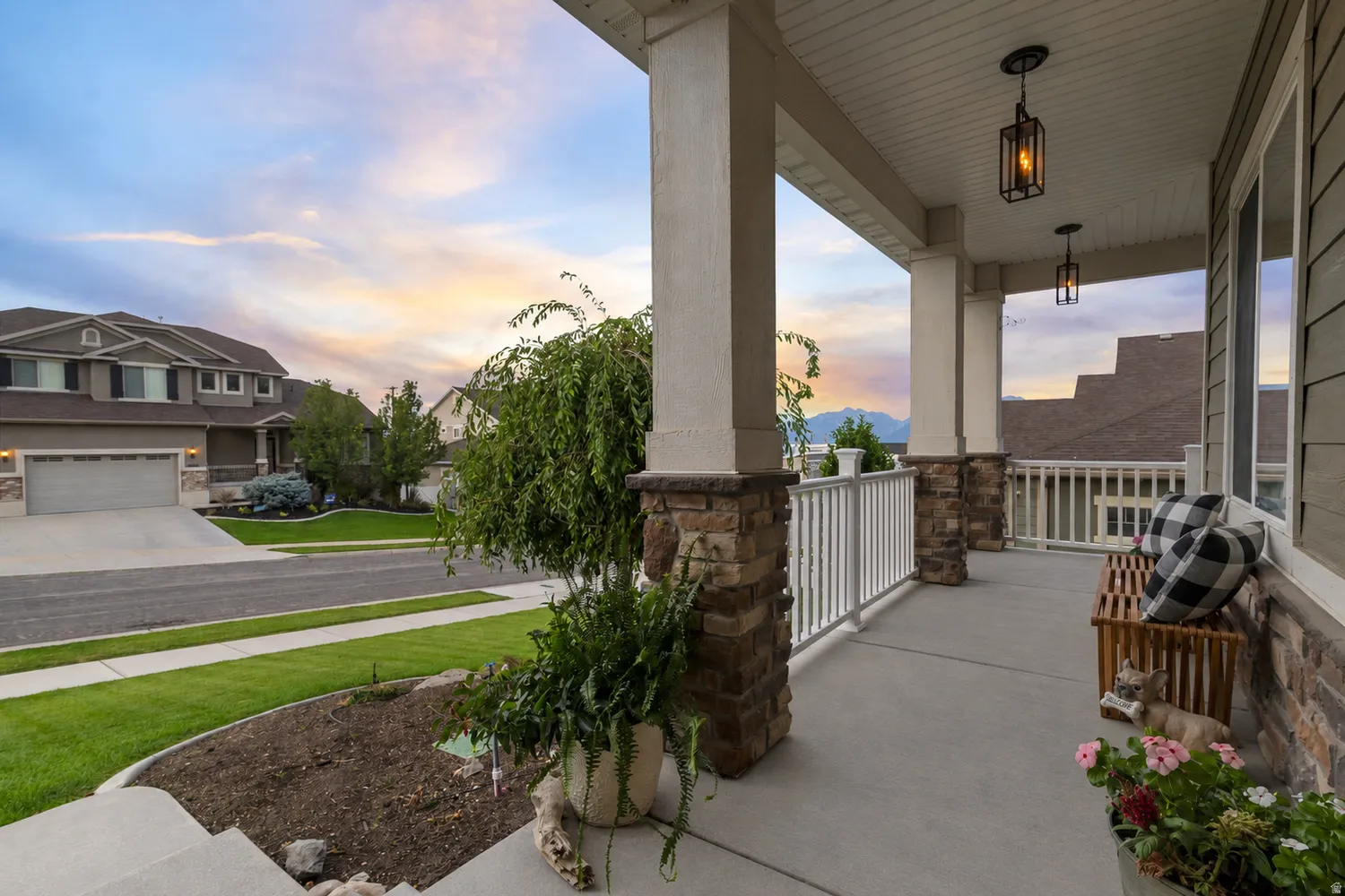 Spacious covered porch with stone-wrapped columns, white railings, and two hanging lanterns