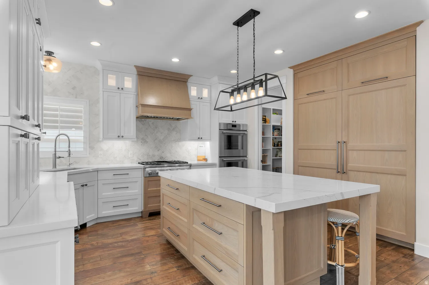 Spacious kitchen featuring an expansive center island with a stone countertop, wood-finish flooring, white cabinetry, a wood-paneled refrigerator, and recessed lighting